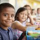 Young boy and girl at school lunch table smiling to camera