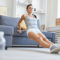 Brunette woman exercising by a sofa in living-room