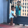 A baby girl stands at the gate communicating with a little boy