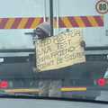 A beggar holding up a joke sign at the traffic lights