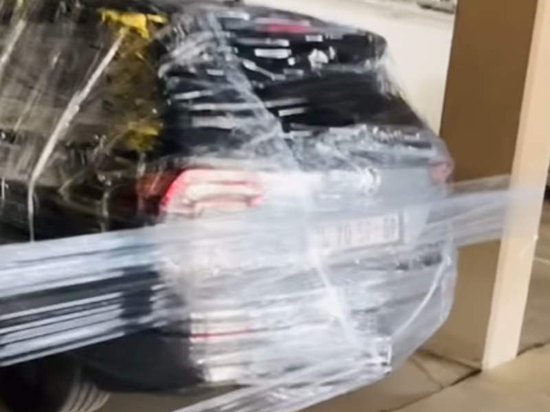 A car is covered in cling wrap parked inside a parking lot