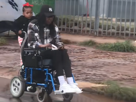 A child rides on the back of her mothers wheelchair on the road