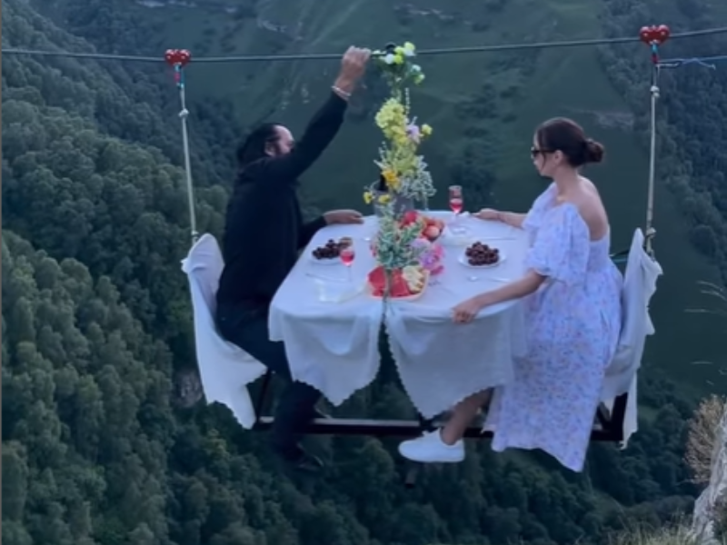 A couple dining on a zipline above a high cliff