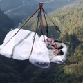 A couple sleep on a bed that is suspended high up between cliffs