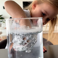 A girl dips her hand into a jar of water with white powder