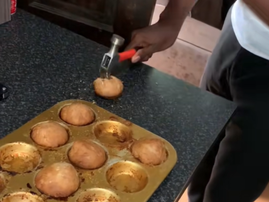 A guy hits a hammer through a muffin in the kitchen