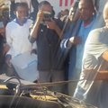 A man pulls a snake out from a vans engine while bystanders watch