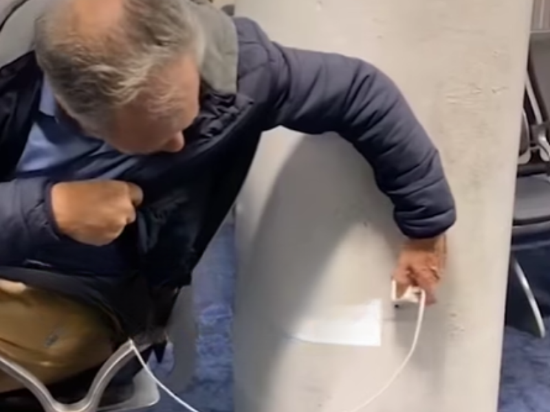 A man trying to plug his phone charger into the wall at an airport
