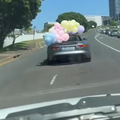 A passenger holds a balloon arrangement out of a convertible car