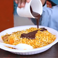 A person pouring chocolate sauce over a plate of biryani