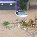 A person sitting on a car that is submerged in water during a flash flood