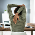 A rear view of a businessman stretching his arms at his desk