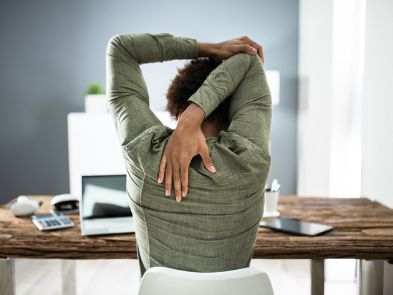 A rear view of a businessman stretching his arms at his desk