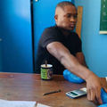 A teacher seated at his desk eating lunch handing a sandwich to a student