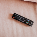 A television remote control lying on pink bed sheet
