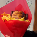 A woman holding a chicken with fries arranged in a bouquet