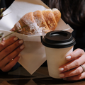 A woman holding a mug of coffee and a croissant
