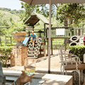 A woman holds a glass of wine while looking at her kids playing at play area in restaurant