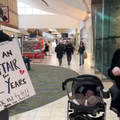 A woman stands next to her baby stroller and shouts while husband wears sign board