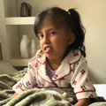 A young girl sitting on her bed holding onto her blanket