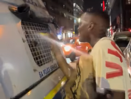 A young man holding KFC takeout talking to people at the back of a police van