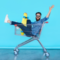 A young man sits inside a shopping cart holding a skateboard