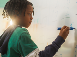 An African boy finding a solution to a Math problem on the whiteboard