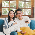 An Asian couple laughing together as they watch something on TV