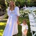 Blonde woman wearing white outfit at a wedding holding her son's hand