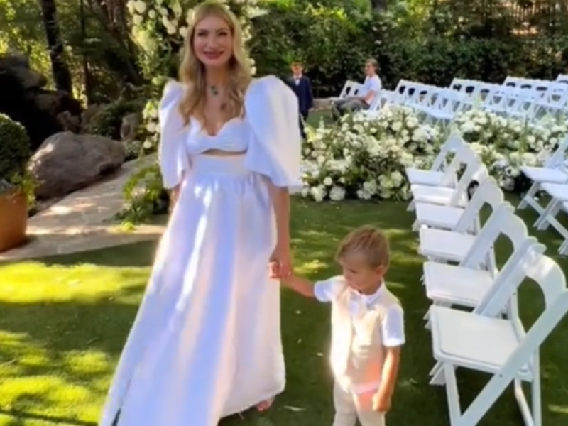 Blonde woman wearing white outfit at a wedding holding her son's hand
