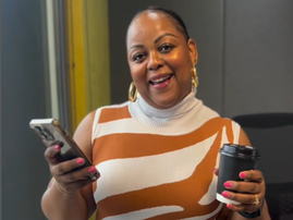 Carol Ofori standing inside the studio with a coffee and her phone