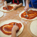 Children making pizza at home with pizza bases and tomato sauce