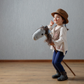 Cute little girl dressed like a cowgirl playing with a stick horse
