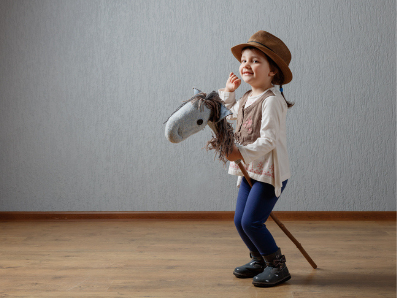 Cute little girl dressed like a cowgirl playing with a stick horse