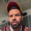 Drake wears a red and yellow baseball cap while taking a selfie