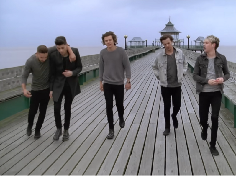 One Direction members walking on a pier