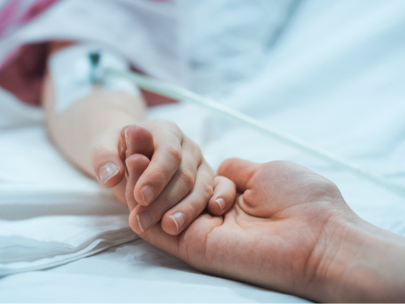 Recovering little child lying in the hospital holding mothers hands