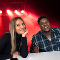 Stacey and J Sbu sitting at a table with stage behind them
