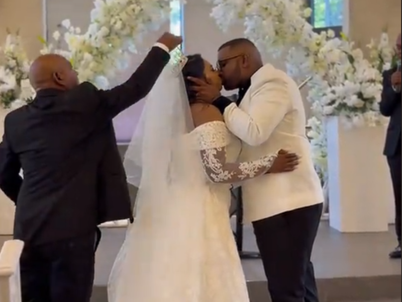 The father of the bride fixes her veil during her first kiss with husband