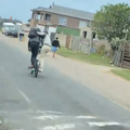 Two friends ride a bike upright with their arms interlocked