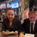 Two ladies sit at a restaurant reading from pieces of paper
