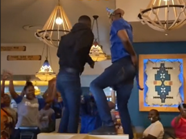 Two restaurant workers dance on the table to entertain customers