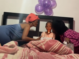 Two women lean in to kiss a young girl as she blows out her birthday candles