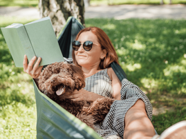Woman relaxing on a hammock with her dog while reading a book