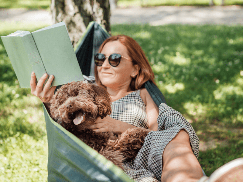 Woman relaxing on a hammock with her dog while reading a book